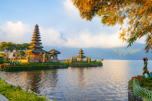 Pura Ulun Danu Bratan temple in Bali island. Beautiful balinese temple. Balinese landmark. Cloudy sky. Water reflection. Foreground with tree branches. Bratan lake, Bedugul, Bali, Indonesia